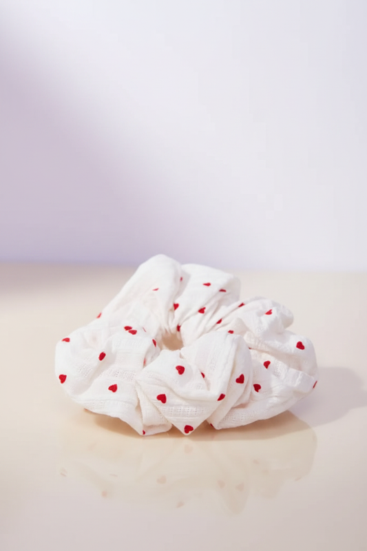 Sweetheart Scrunchie auf heller Oberfläche mit zartem Pastell-Lichtschimmer im Hintergrund