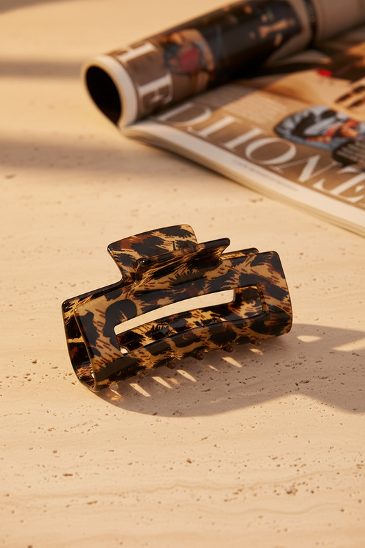 Square Safari Clip auf Sand-Travertin-Oberfläche mit Mode-Magazin im Hintergrund