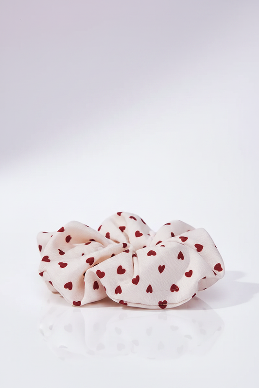Amour Scrunchie auf heller Oberfläche mit zartem Pastell-Violett-Lichtschimmer im Hintergrund